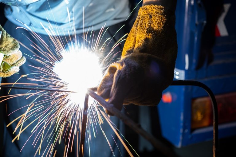 Young man with protective mask welding in a factory