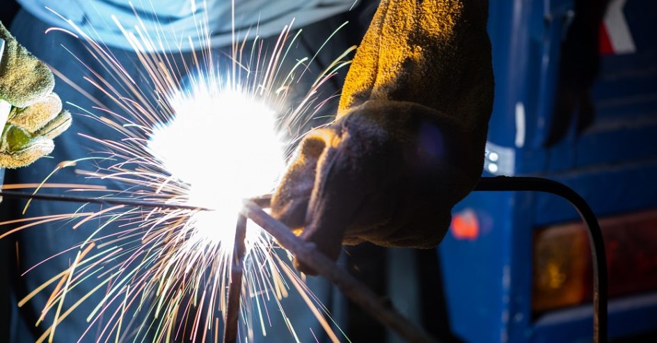 Young man with protective mask welding in a factory
