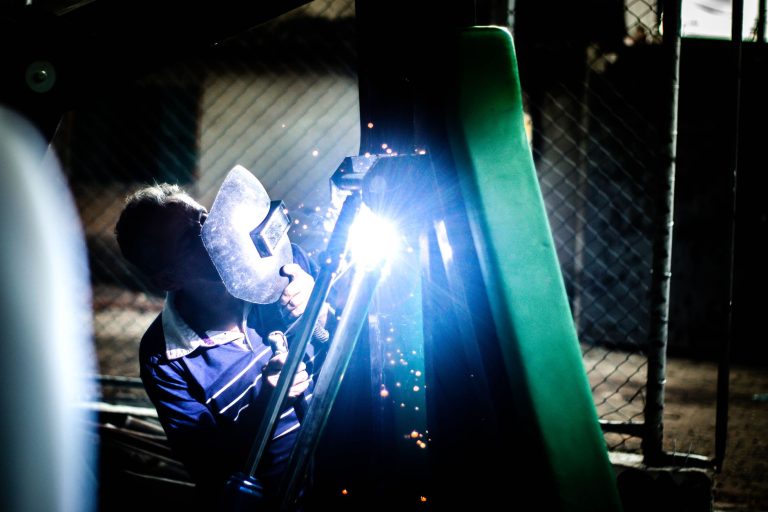 Welder repairing metal fencing with sparks at night