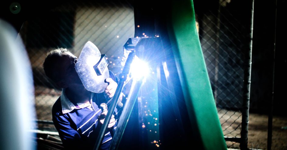 Welder repairing metal fencing with sparks at night