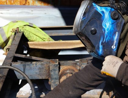 Mobile welder in a helmet welding a steel trailer frame on site outdoors