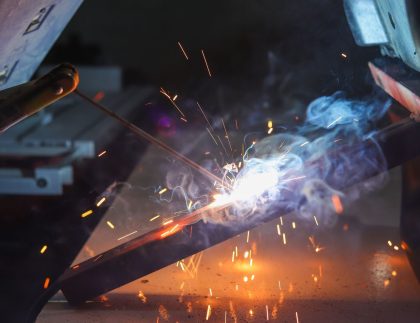 Welder striking an arc on a steel bar with sparks and smoke in a commercial shop