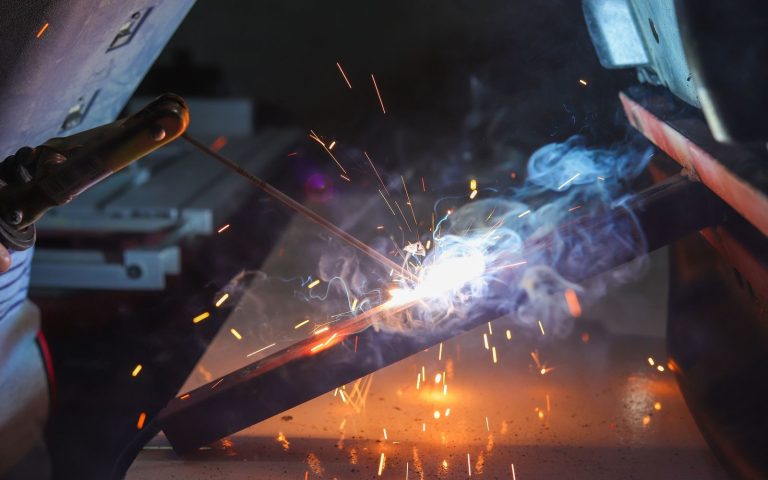 Welder striking an arc on a steel bar with sparks and smoke in a commercial shop