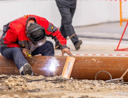 Welder in protective gear stick-welding a steel pipe at an outdoor job site