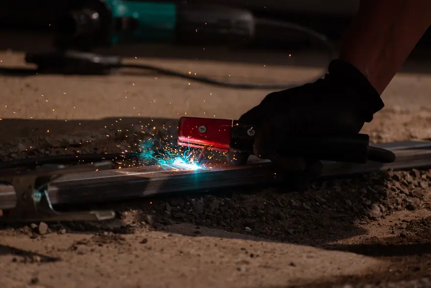 Gloved hand stick-welding a steel bar on the ground with sparks flying