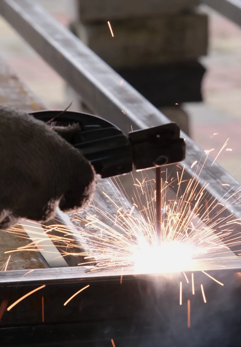 Gloved hand holding an electrode holder as sparks fly from a weld on a steel frame