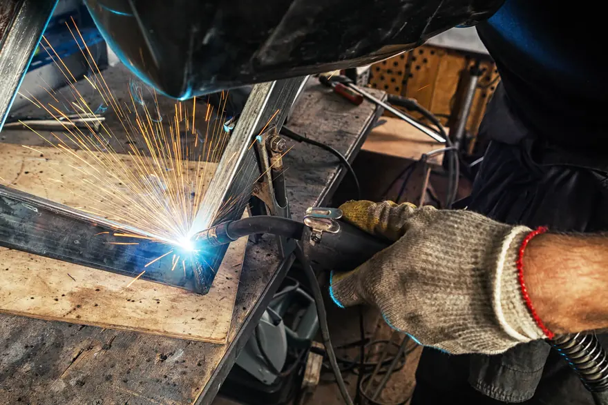 Gloved hands MIG welding the corner of a custom steel frame