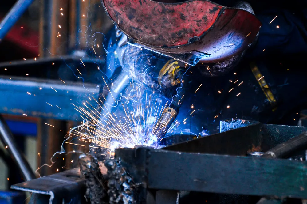 Welder in a red helmet welding a metal table frame as blue sparks spray