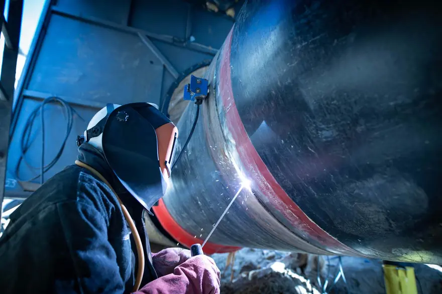 Welder in a helmet running a bead along a large steel pipeline section
