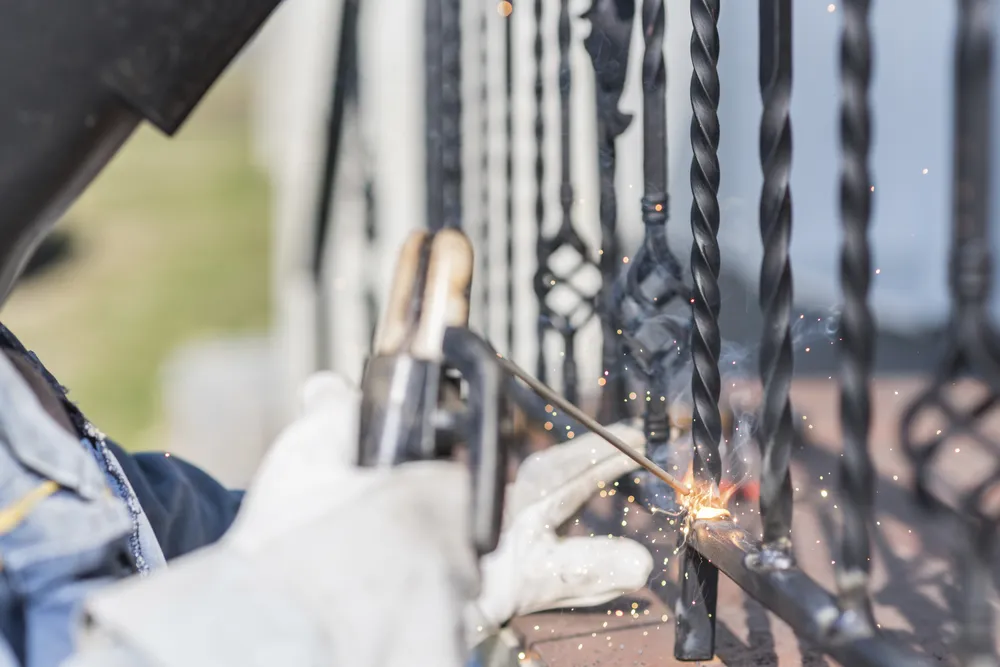 Gloved hand welding the base of twisted wrought iron railing bars