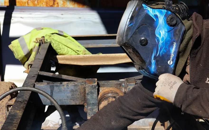 Mobile welder in a helmet welding a steel trailer frame on site