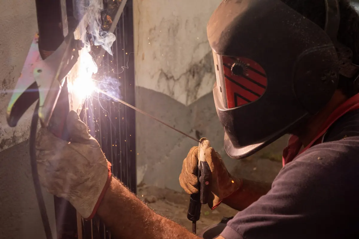 Welder in a helmet stick-welding a metal frame in a doorway, arc light glowing