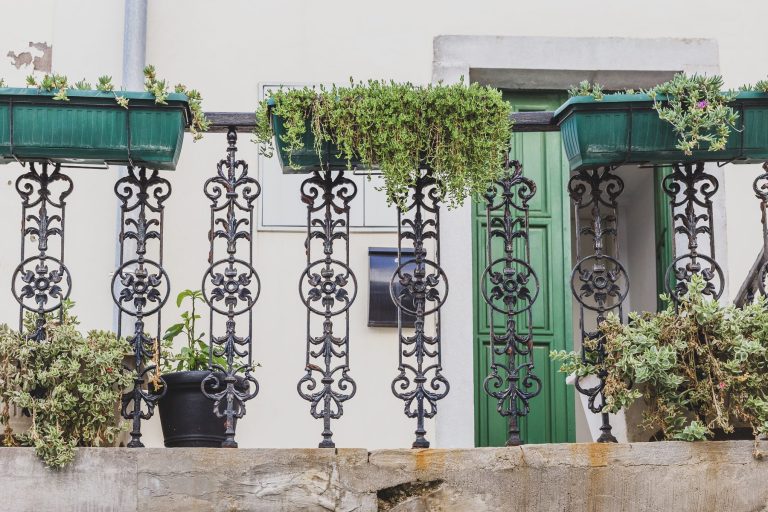 Ornate black iron balcony railing lined with potted plants