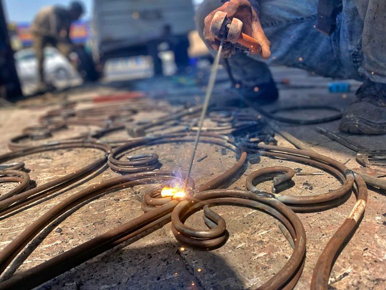 Welder joining curved scroll pieces of ornamental ironwork